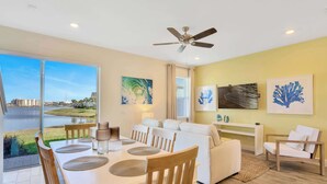 A spacious living area with a dining table, white sofas, and a ceiling fan. - Sunkissed at Margaritaville - Serene Lake Views (Kissimmee)