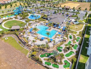 Vista aérea de un complejo turístico con una piscina grande, varias zonas de descanso y un campo de golf.