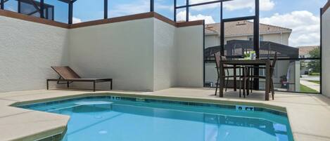 Une piscine entourée de parois en verre, une chaise longue et une table avec des chaises.