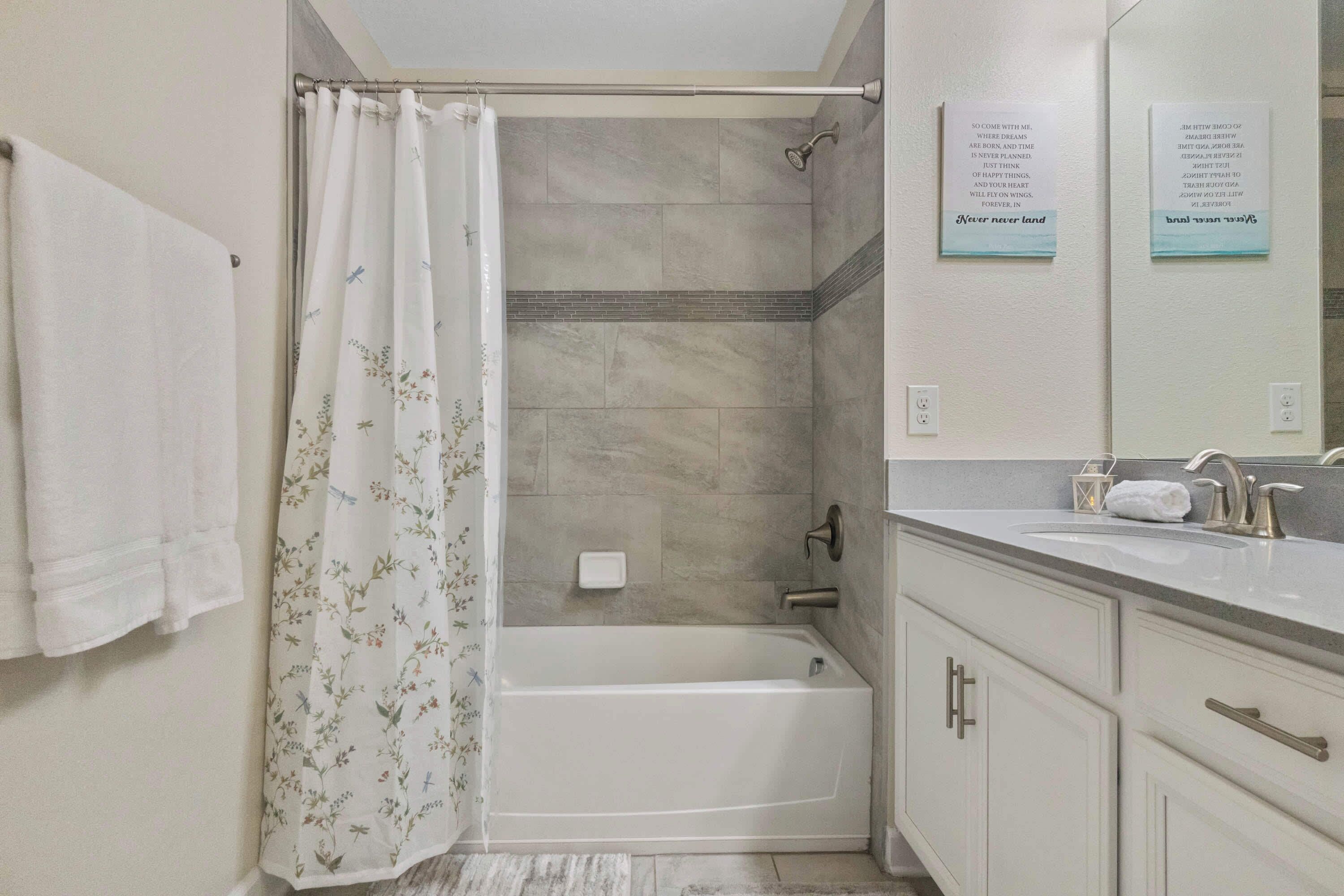 A bathroom with a shower curtain, a bathtub, a vanity with a mirror, and a towel rack.
