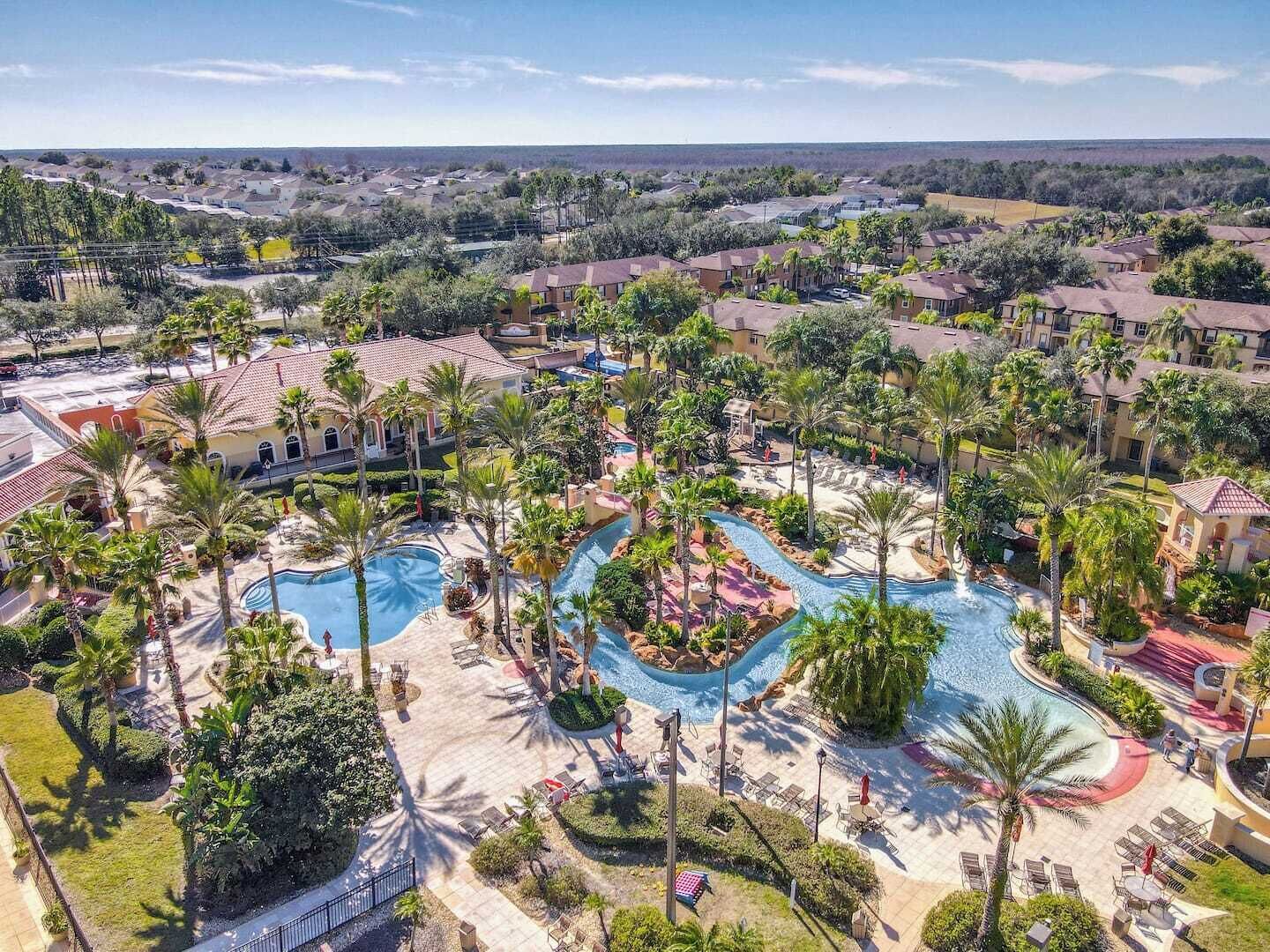 A resort with multiple swimming pools, palm trees, and a view of the surrounding residential area.