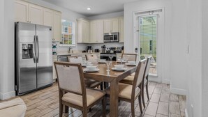 A modern kitchen with white cabinets, stainless steel appliances, and a dining area with a wooden table and chairs.