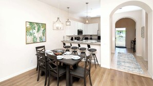 A modern kitchen with white cabinets, a dining area with a dark wooden table and chairs, and a hallway with a blue patterned rug. - Family Ties at Bahama Bay - Luxe 3BR Townhouse (Davenport)