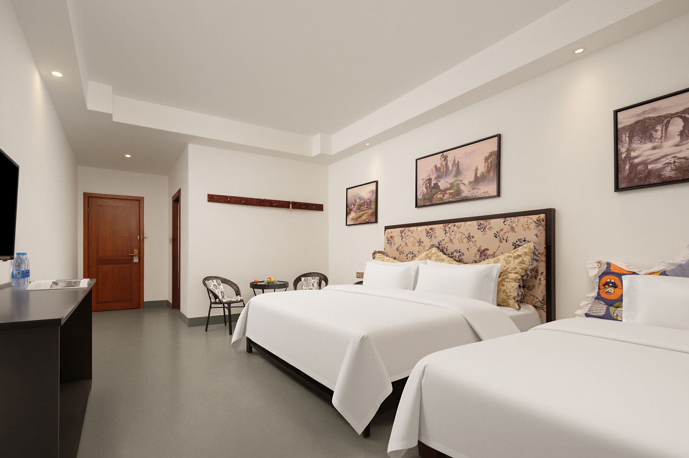 Een hotelkamer met twee bedden, een bureau, een stoel en kunstwerken aan de wanden.
