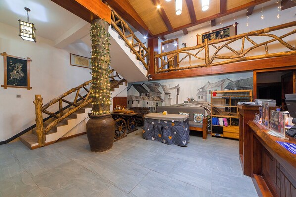 Un intérieur rustique avec un escalier en bois, un grand vase illuminé et une table recouverte d’une nappe à carreaux.