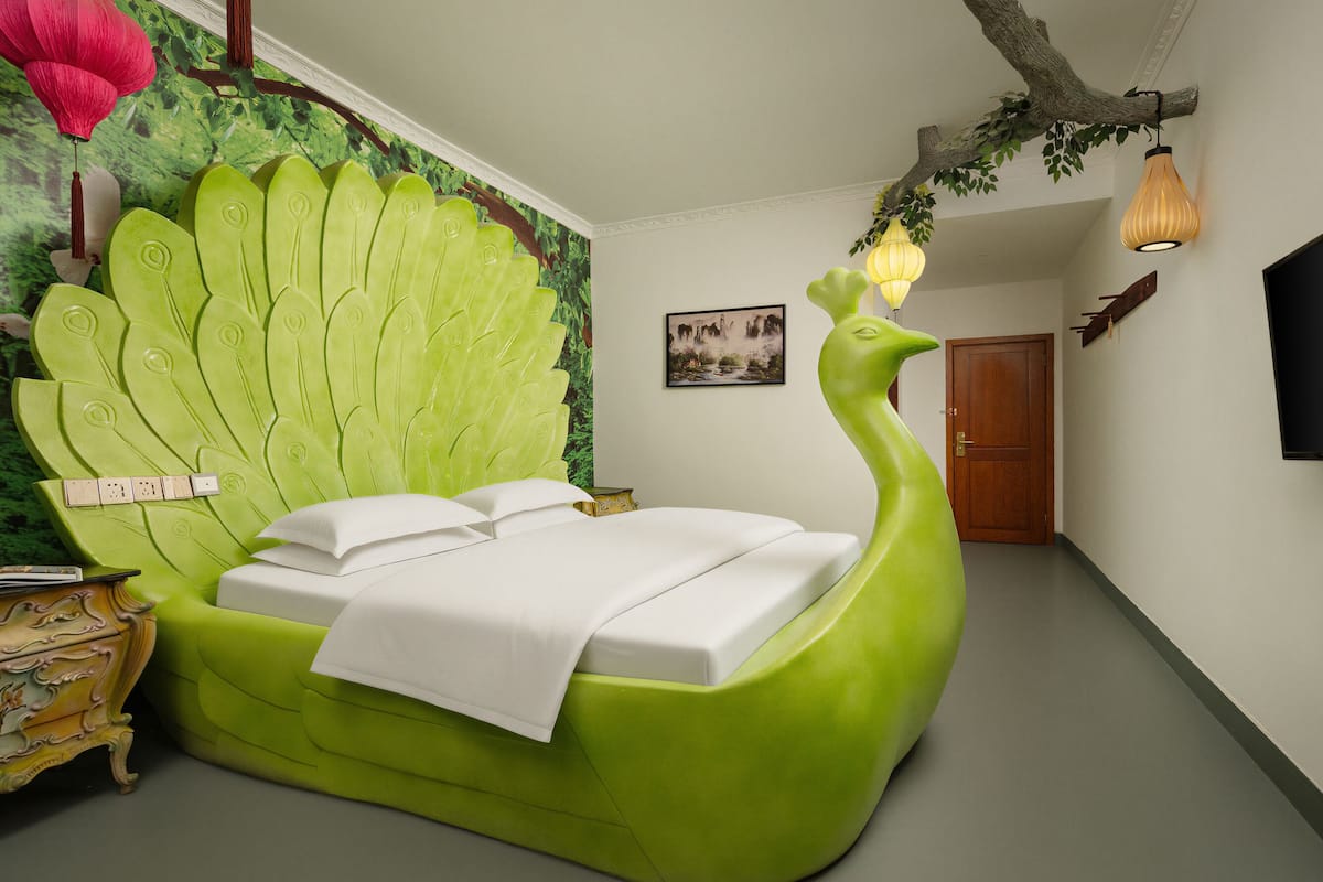 Une chambre au design unique, avec un lit aux couleurs vertes, inspiré du plumage du paon, une petite table d’appoint et une porte.