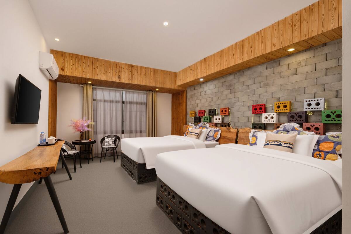 Une chambre d’hôtel avec deux lits, un bureau en bois, une télévision et un mur décoré d’un motif en briques.