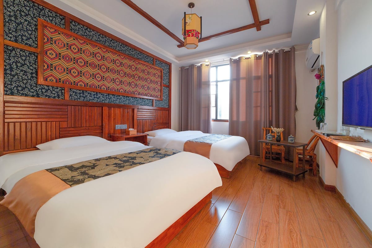 Une chambre d’hôtel avec deux lits, une tête de lit en bois, un grand mur décoratif, une petite table avec des chaises et un téléviseur.