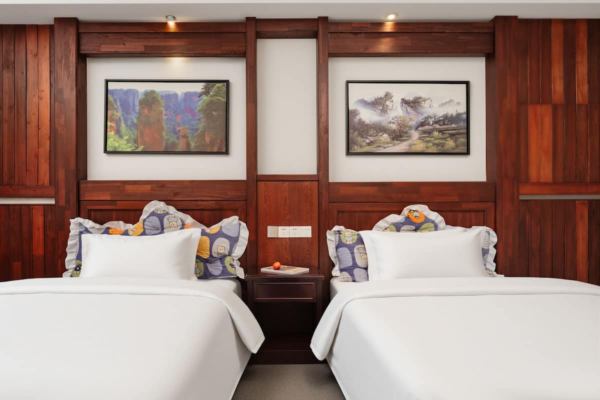 Une chambre d’hôtel avec deux lits, un lambris en bois et deux tableaux représentant des paysages, encadrés.
