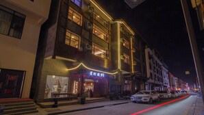 A two-story building with a traditional facade, illuminated by warm interior lighting. - Zhangjiajie Xinghe Qingmeng Folk-style Inn (Zhangjiajie)