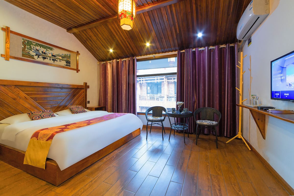 Une chambre d’hôtel avec un grand lit, un bureau avec une chaise, une télévision et une fenêtre avec des rideaux.