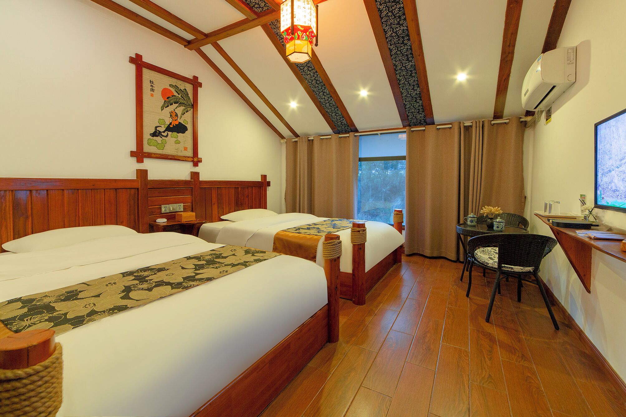 Habitación de hotel con dos camas, un escritorio, una silla, un ventanal con cortinas y una obra de arte tradicional en la pared.