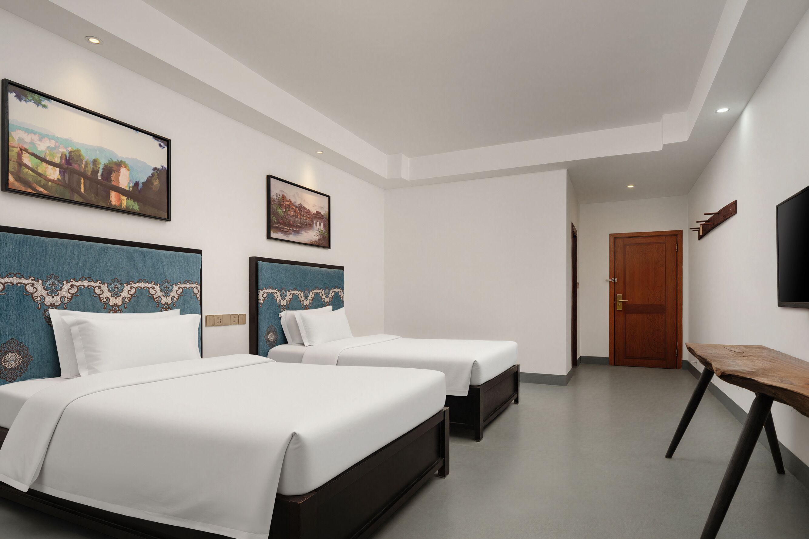 A hotel room with two beds, a wooden table, a TV, and artwork on the walls.