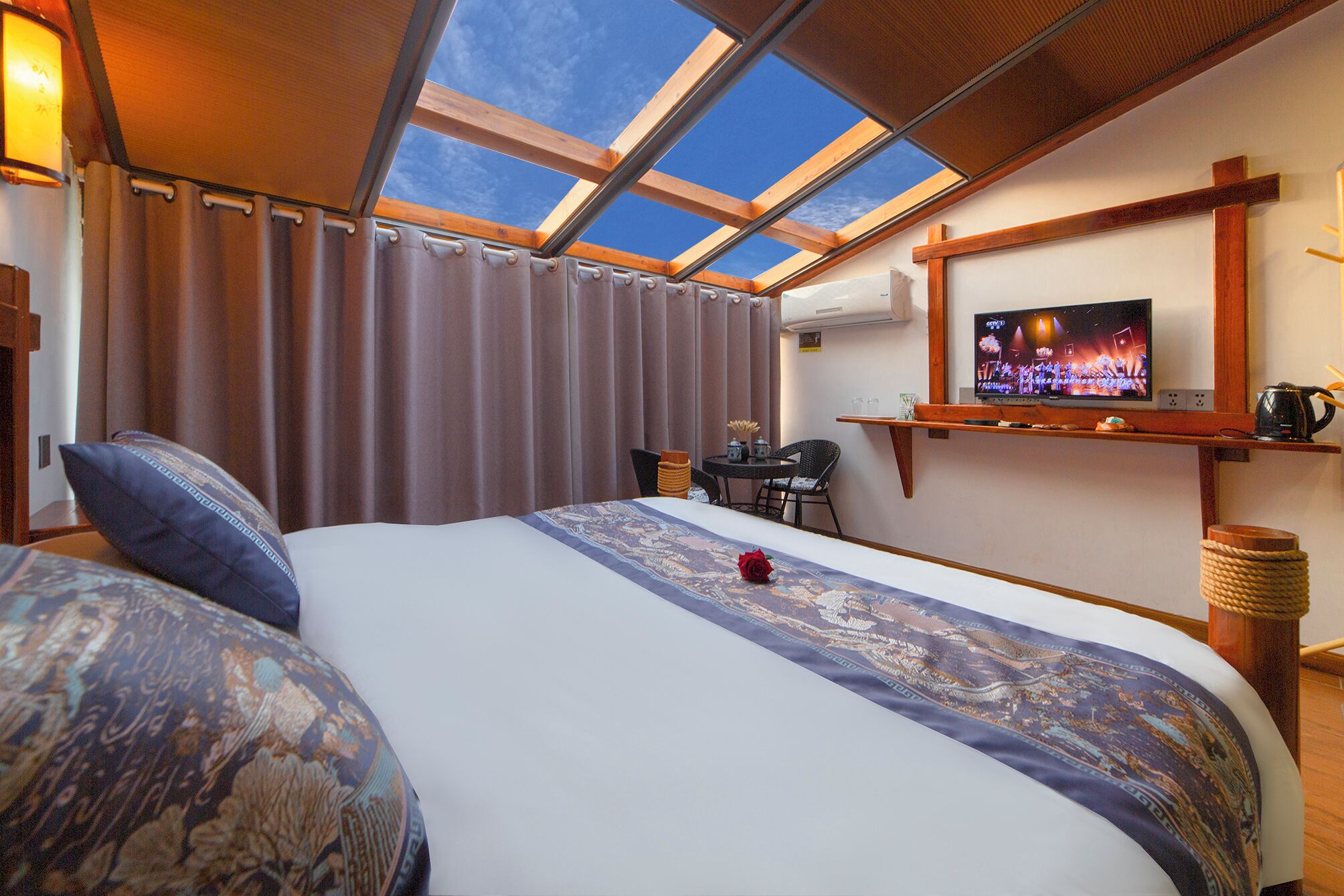 A hotel room with a large bed, a desk, a television, and a skylight.