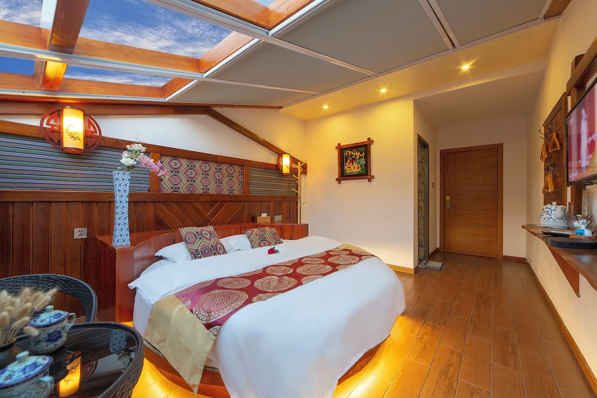 Une chambre avec un grand lit, une tête de lit en bois, un puits de lumière, un téléviseur fixé au mur et un plancher en bois.
