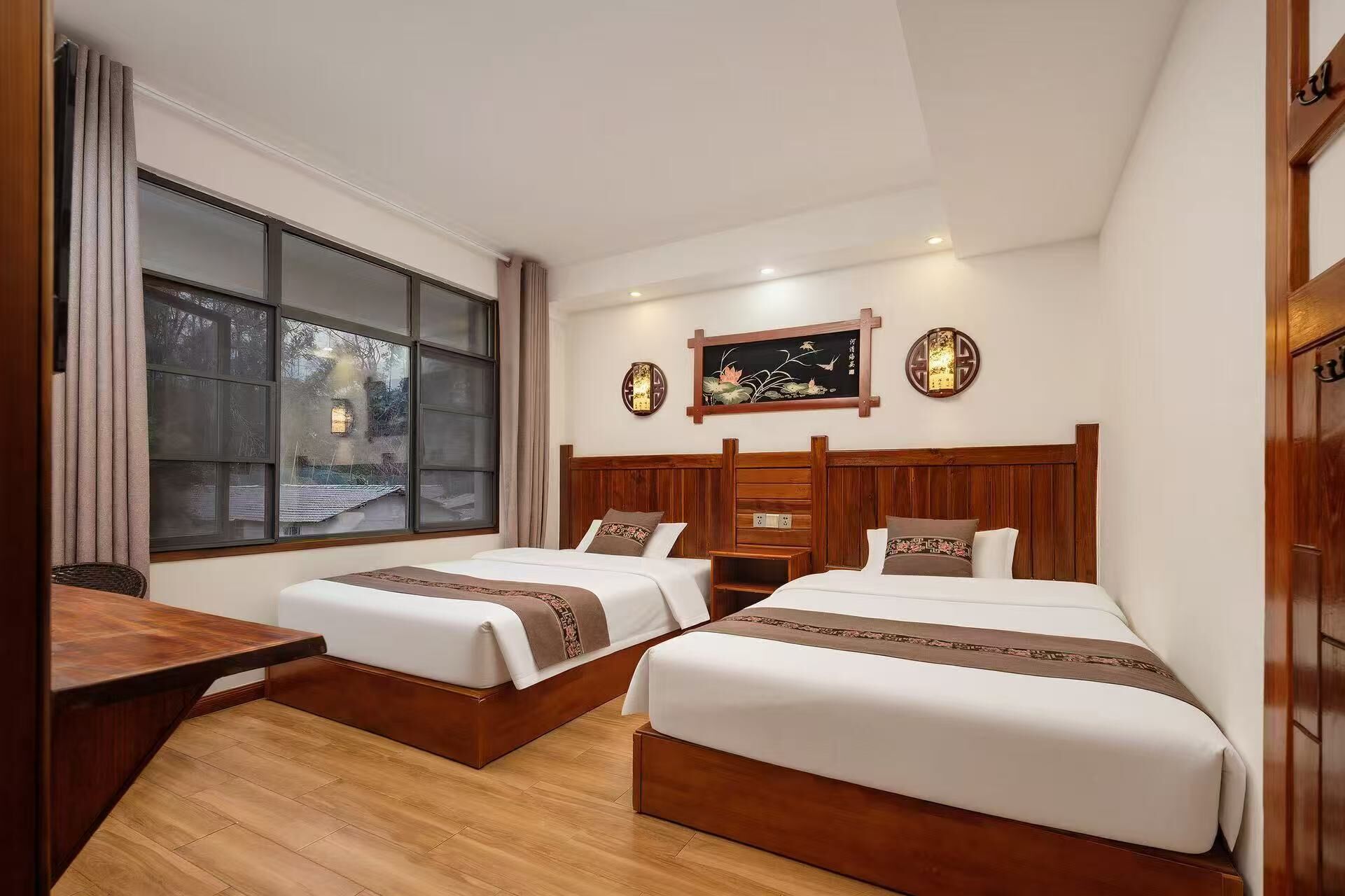 Une chambre d’hôtel avec deux lits, un bureau en bois, une grande fenêtre et un décor traditionnel.