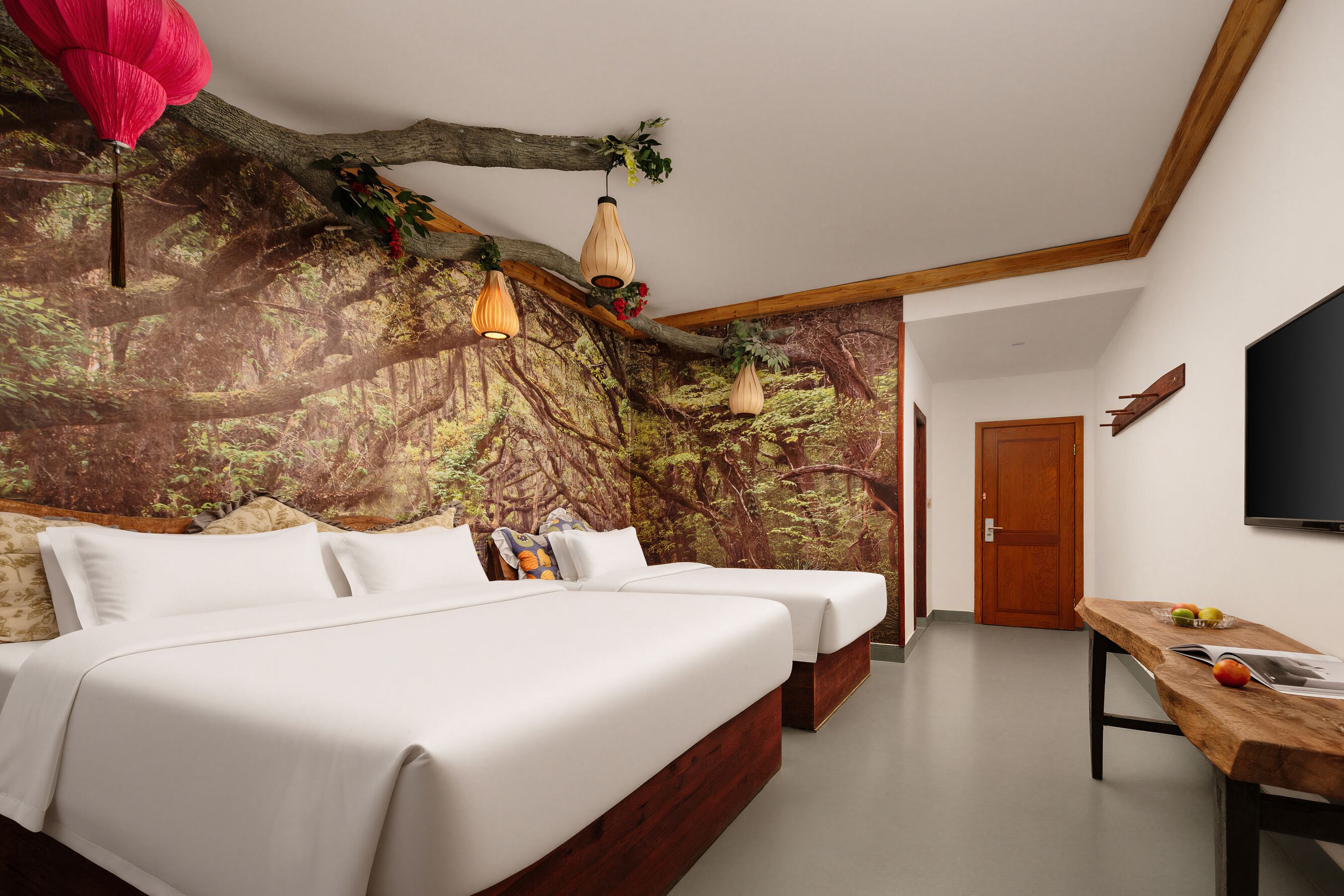 A bedroom with a large bed, two bedside tables, a wooden desk, and a mural of a forest on the wall.