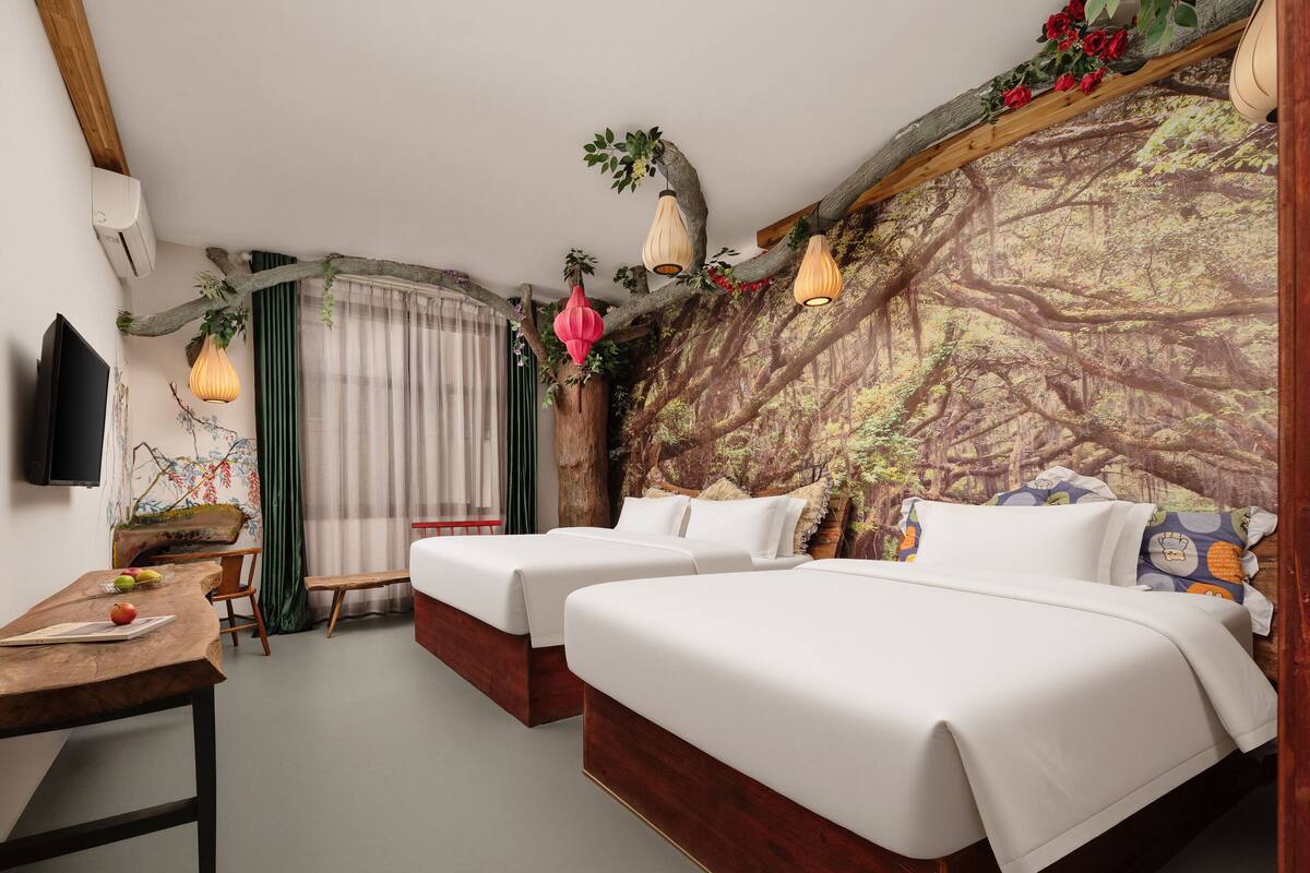 Une chambre d’hôtel avec deux lits, un bureau, une chaise, une télévision et un mur décoré sur le thème de la forêt.