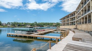 Ein Hotel am Wasserufer mit einer hölzernen Anlegestelle, die sich über ruhiges Wasser erstreckt, einem überdachten Boot und einem Gebäude mit Balkonen.