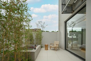 Un patio moderno con una jardinera de hormigón, un taburete de madera y una silla de mimbre.