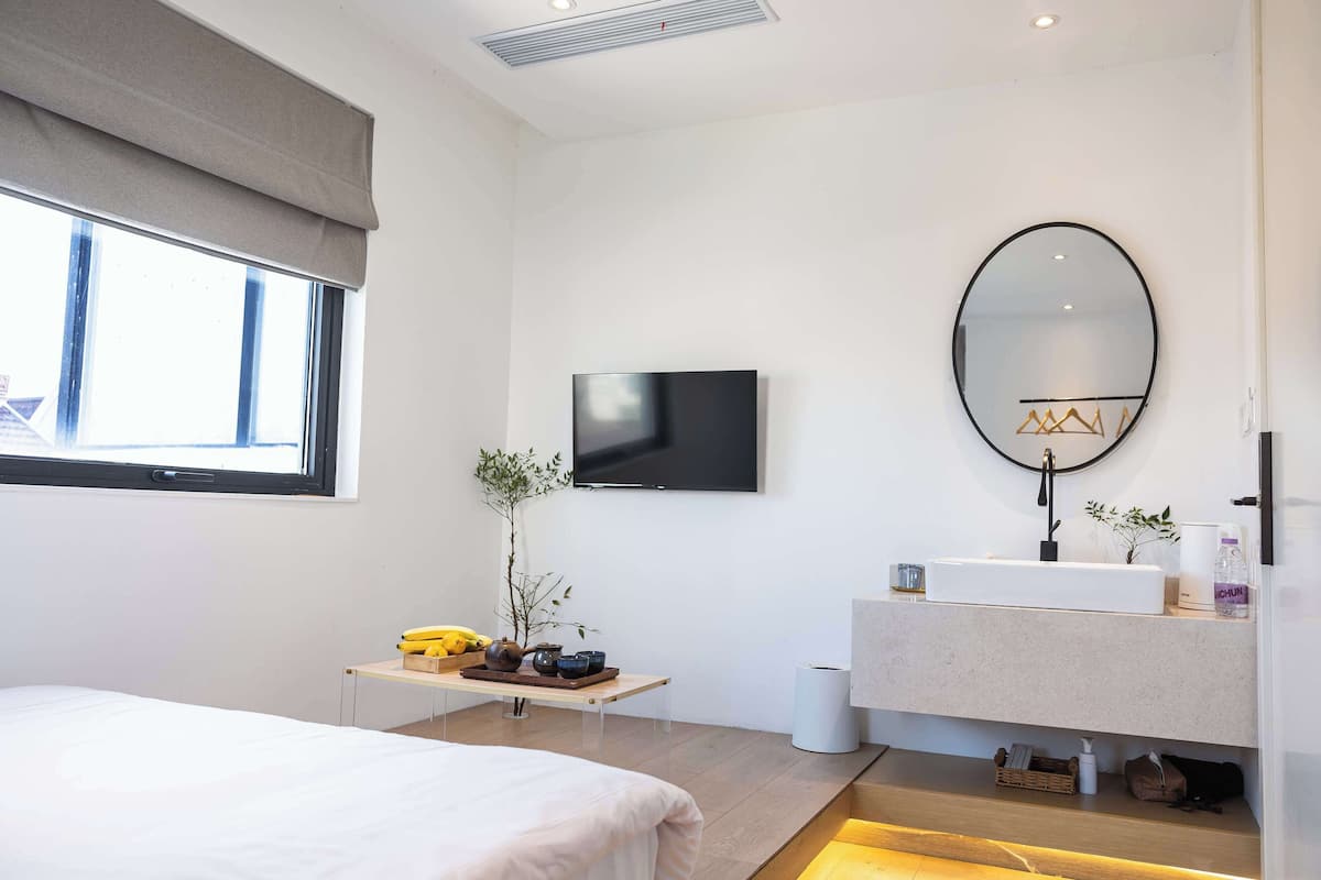 A modern bedroom with a bed, bedside table, TV, and a bathroom with a sink and mirror.