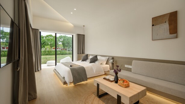 Habitación de hotel moderna con una cama grande, un sofá, una mesita de centro y un cuadro en la pared.