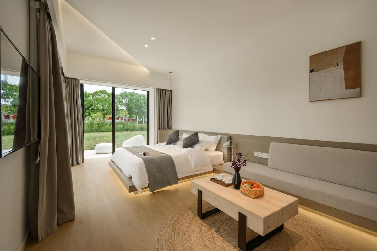 A modern hotel room with a large bed, a sofa, a coffee table, and a painting on the wall.
