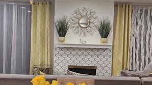 A modern living room with a sofa, a coffee table with yellow roses, a fireplace with decorative mirrors, and patterned curtains. - Beach • Pools • Comfort:  Private Room + Bath Prime LA Location (Los Angeles)