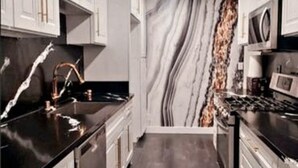 A modern kitchen with white cabinets, a black countertop, and a marble backsplash. - Beach • Pools • Comfort:  Private Room + Bath Prime LA Location (Los Angeles)
