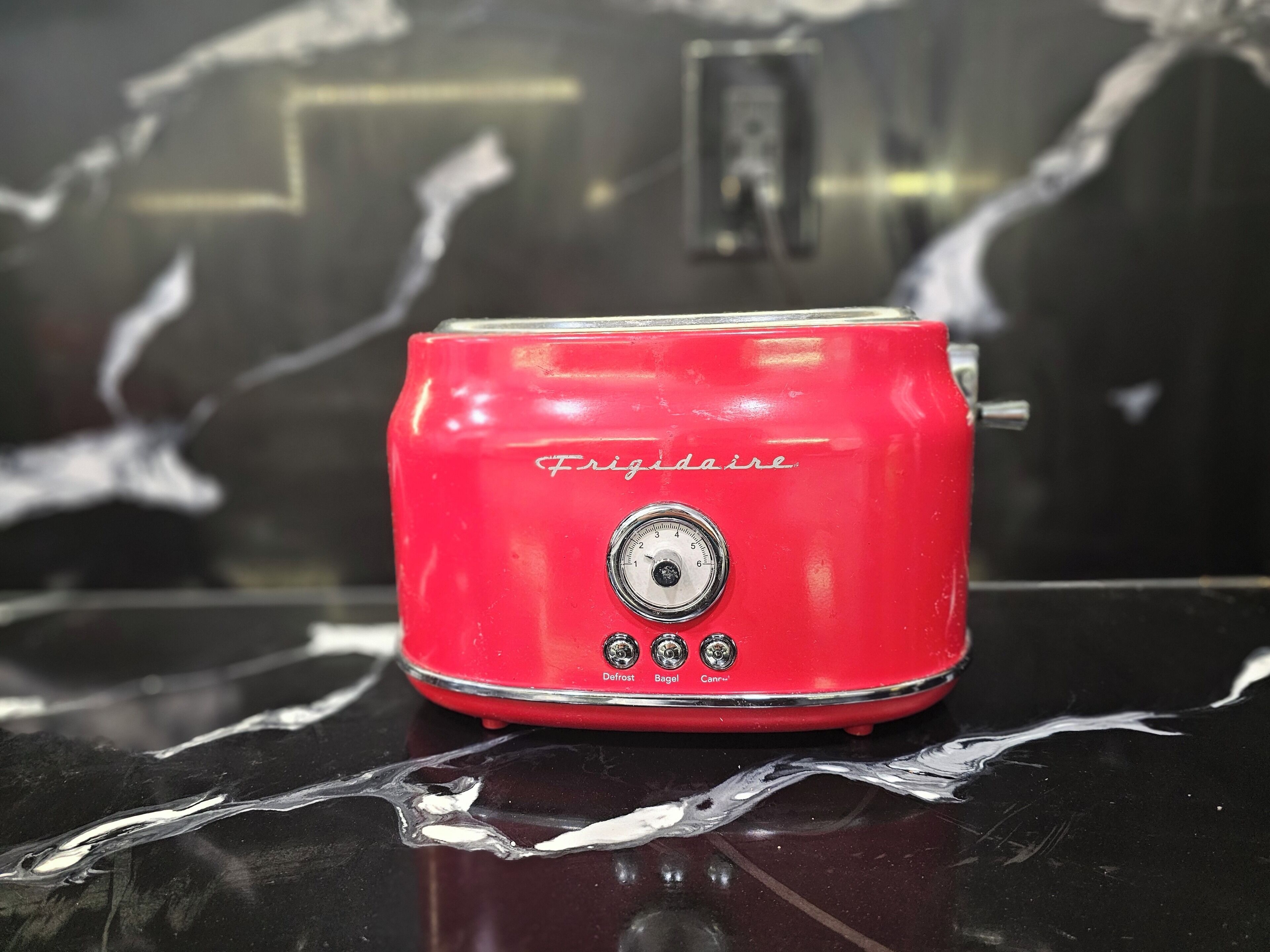 A red Frigidaire toaster on a reflective black surface.