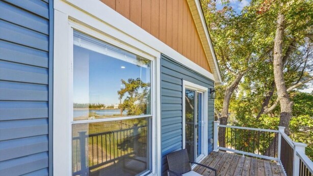 A house with a wooden deck, large windows, and a view of a lake.