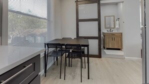 A modern kitchen with a dining area, a sliding barn door, and a small bathroom with a sink and mirror.