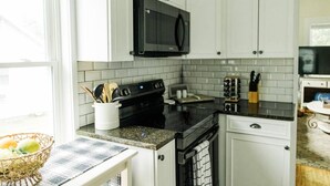 Una cocina con armarios blancos, un microondas negro, una estufa y un lavamanos.