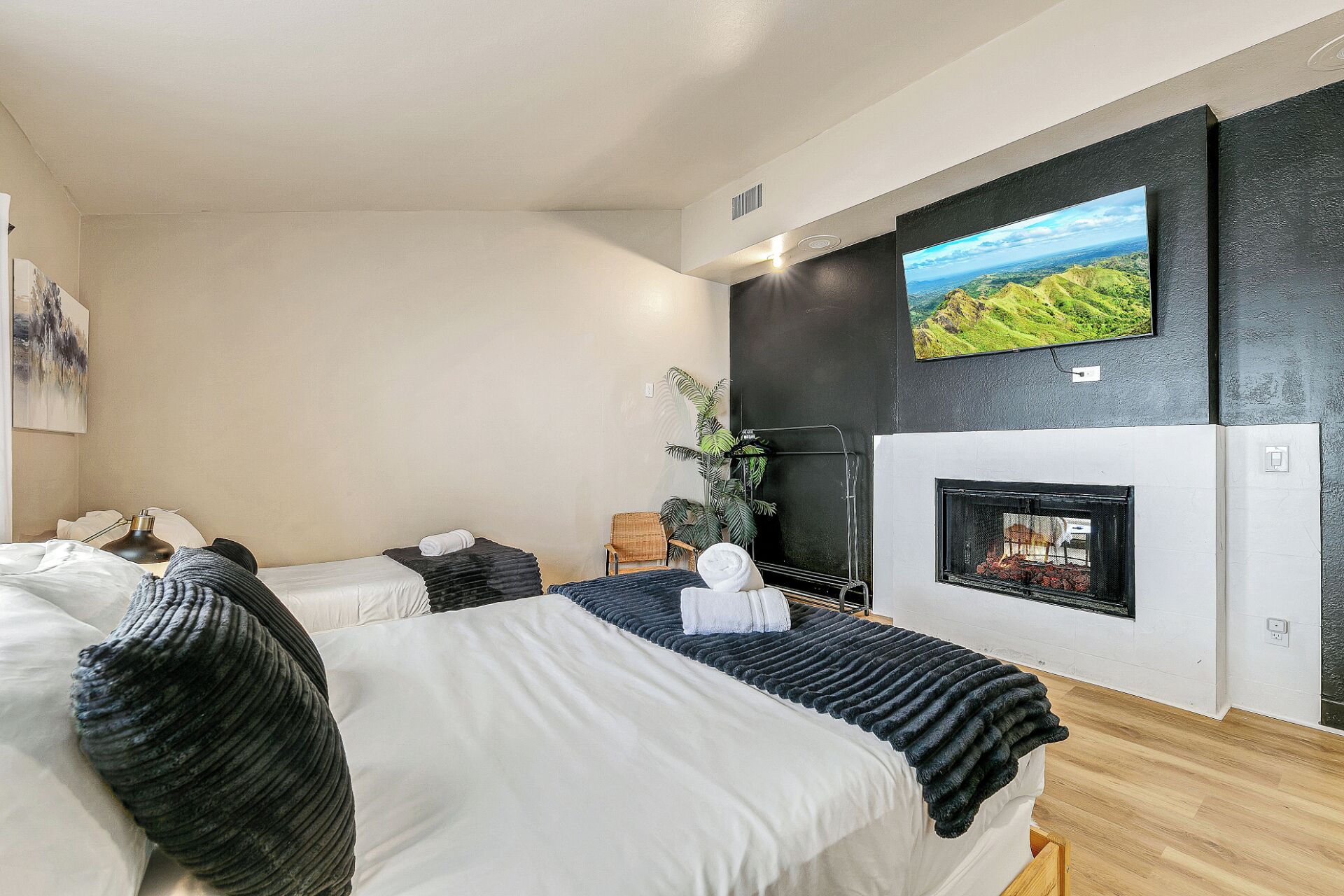 Habitación de hotel moderna con una cama grande, chimenea, televisión montada en la pared y vistas a un paisaje.