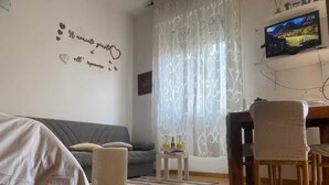 Ein Wohnzimmer mit Sofa, Couchtisch, Sessel und Fernseher an der Wand.