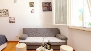 Ein modernes Wohnzimmer mit einem grauen Sofa, einem kleinen weißen Tisch mit Getränken und einem Fenster mit Vorhängen.