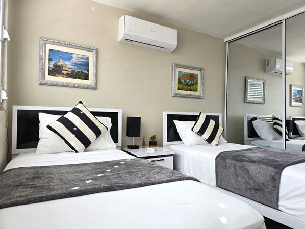 A hotel room with two beds, a bedside table with a lamp, and framed pictures on the wall.