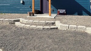 A two-story building with a dark blue exterior and a red roof. There is a porch with wooden columns and a door. A sign on the ground reads "Parkside Unit B". - Parkside Nest Apartment Near Manito Park (Spokane)