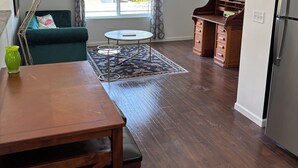 A spacious loft with a high ceiling, a dining area with a wooden table and chairs, a cozy green sofa, a small round table, and a kitchen area with a refrigerator. - Parkside Nest Apartment Near Manito Park (Spokane)