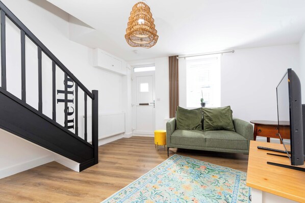 Una sala moderna con una escalera, un sofá, un televisor y un tapete decorativo.