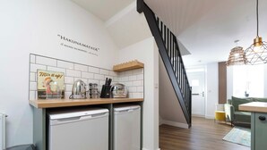 A compact kitchen with a wooden countertop, two white appliances, and a sign that reads "Mix it up!". A black staircase leads to a dining area with a yellow ottoman. - Cosy-cute Miner's Cottage on the Taff Trail (Merthyr Tydfil)