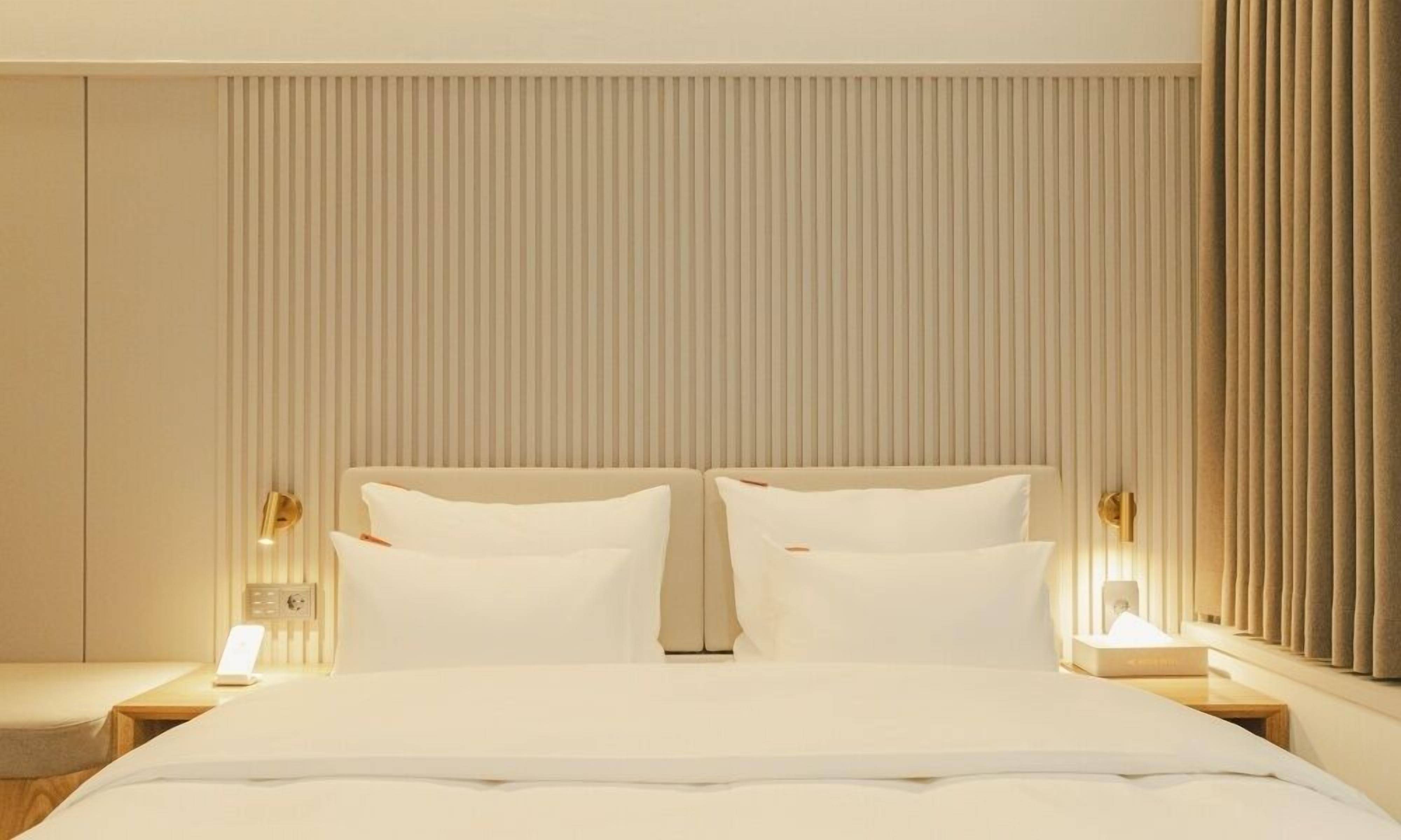 A hotel room with a large bed, two bedside tables, and a wall with vertical blinds.