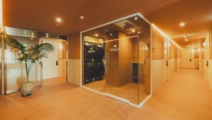 Ein Hotelgang mit Glastürlifter, Zimmerpflanze und Gepäckwagen.