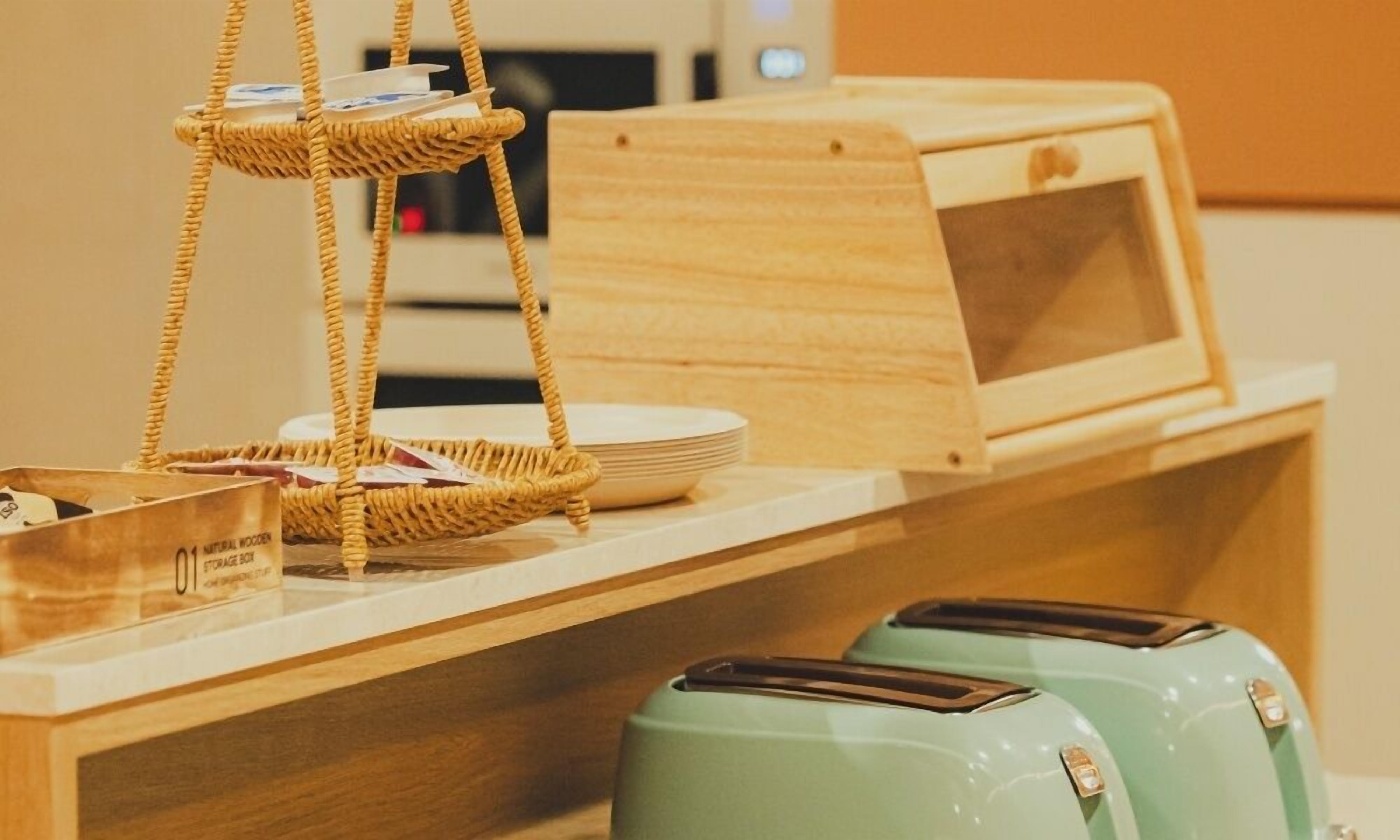 A wooden counter with a woven basket, a stack of plates, and two green toasters.