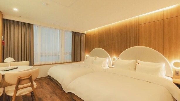 Ein Hotelzimmer mit zwei Betten, einem Schreibtisch mit Stuhl und einem großen Fenster mit Vorhängen.