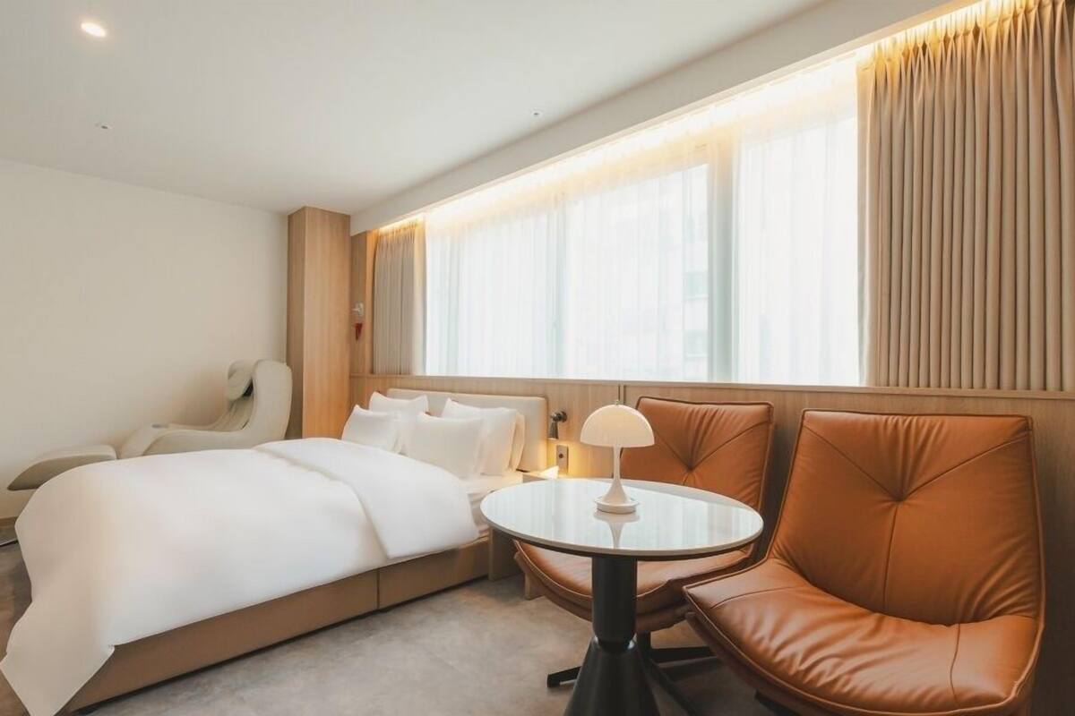 Habitación de hotel con cama, sillón de masajes, una mesa redonda y ventana con cortinas.