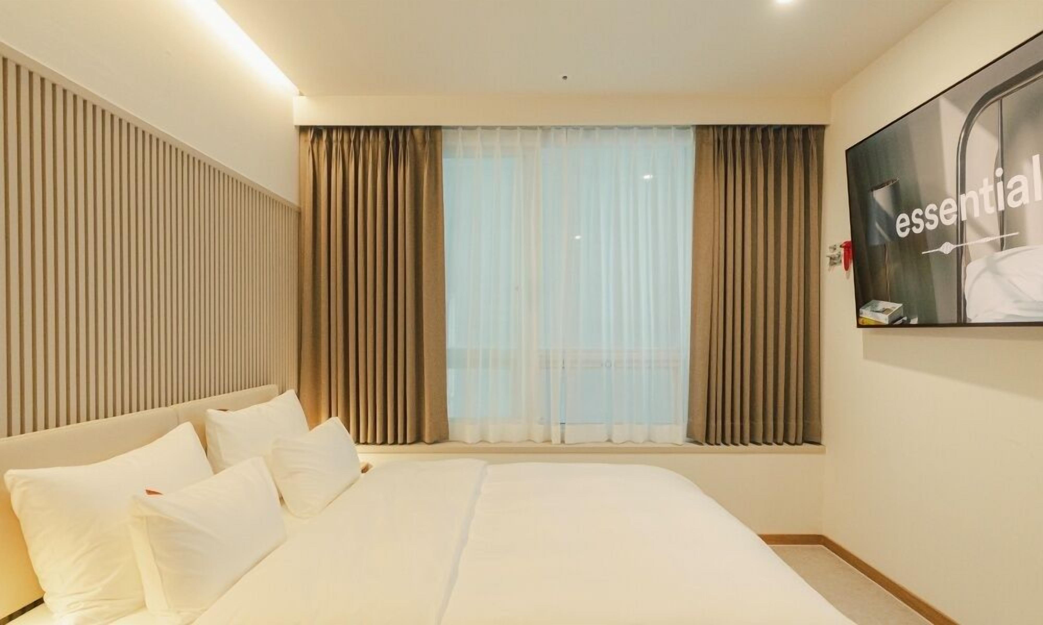 Een hotelkamer met een groot bed, een aan de muur bevestigde televisie en een raam met gordijnen.
