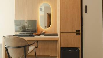 Una habitación de hotel compacta con escritorio de madera, una computadora, una silla, un espejo y un refrigerador.