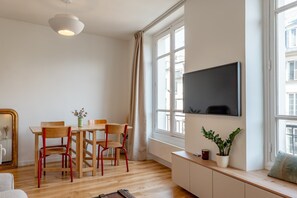 Ein modernes Wohnzimmer mit Esstisch, Stühlen, einem an der Wand befestigten Fernseher und einem Fenster mit Vorhängen.