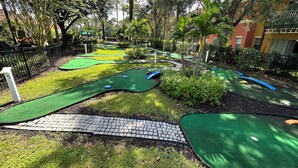 Un campo de mini golf con obstáculos verdes y azules, rodeado de árboles y una valla.
